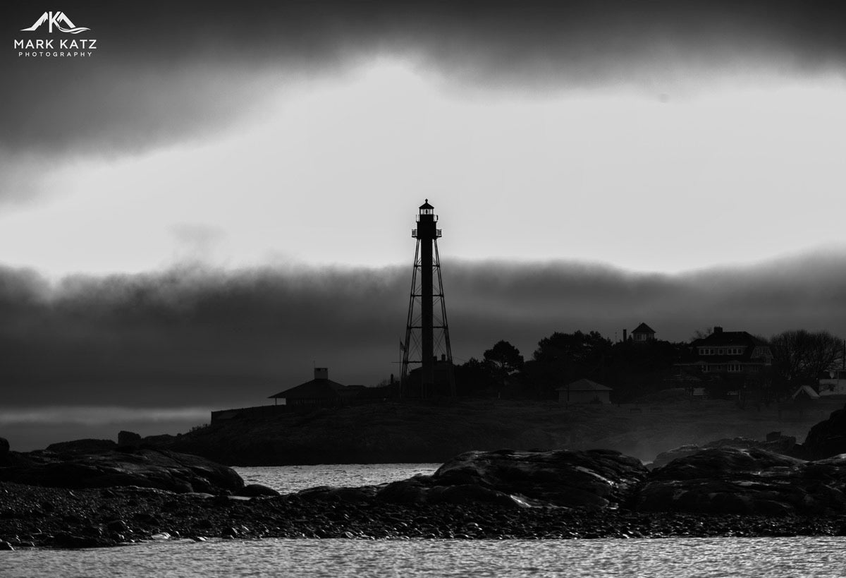 Lighthouse beam shining across dark ocean waters, atmospheric maritime fine art photograph for wall decor.