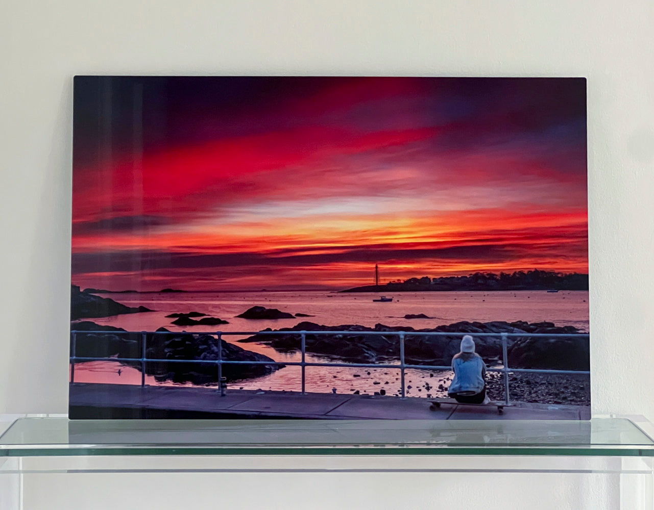 Person sitting on a skateboard watching a vibrant sunrise over Marblehead Harbor