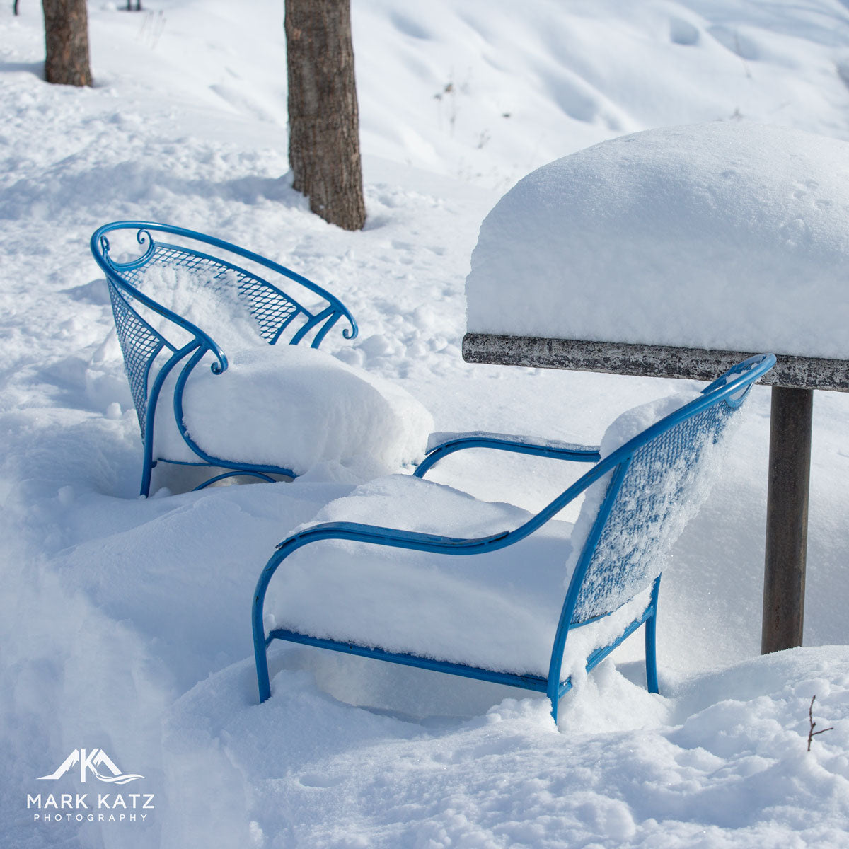 Two blue metal chairs partly buried in deep snow