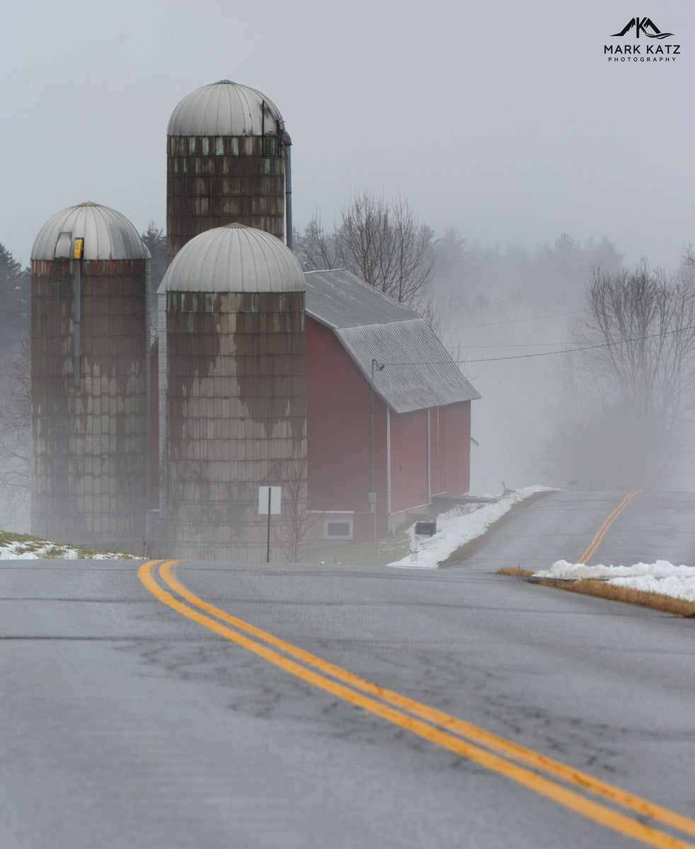Country dirt road winding through foggy winter landscape, fine art photography of rural back roads.
