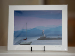 Matted print of a sailboat and lighthouse on Lake Champlain with the Adirodacks in the background.