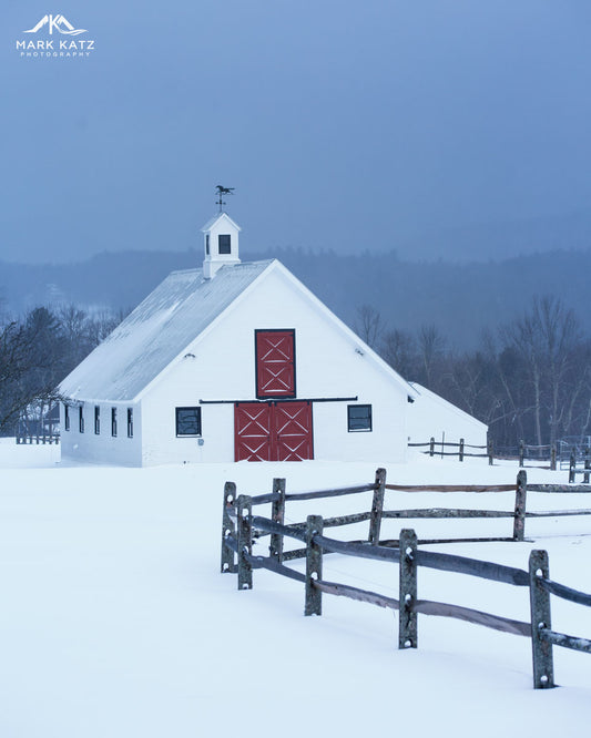 Patriotic Vermont barn painted red with snowy white roof under bright blue sky, fine art decor.