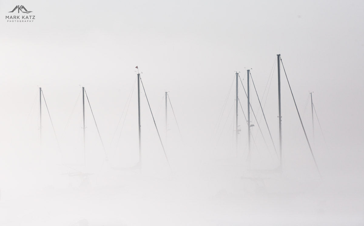 Sailboats barely visible through dense fog, nautical fine art photography capturing marine mystery.