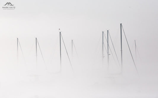 Sailboats barely visible through dense fog, nautical fine art photography capturing marine mystery.