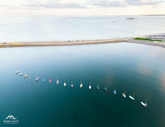Colorful townie sailboats glowing like gemstones on harbor water, vibrant nautical fine art photography print.