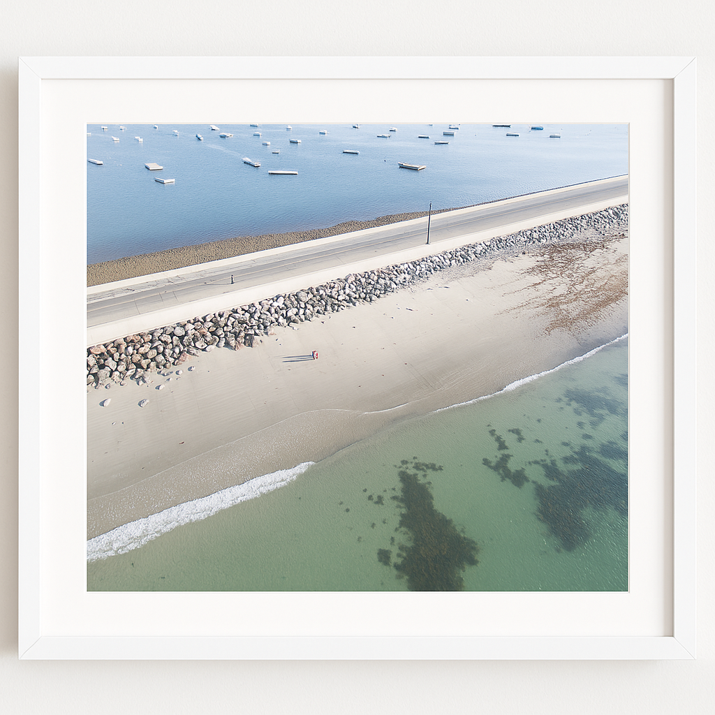 Framed beach print with boats in the water and people walking on the sand.