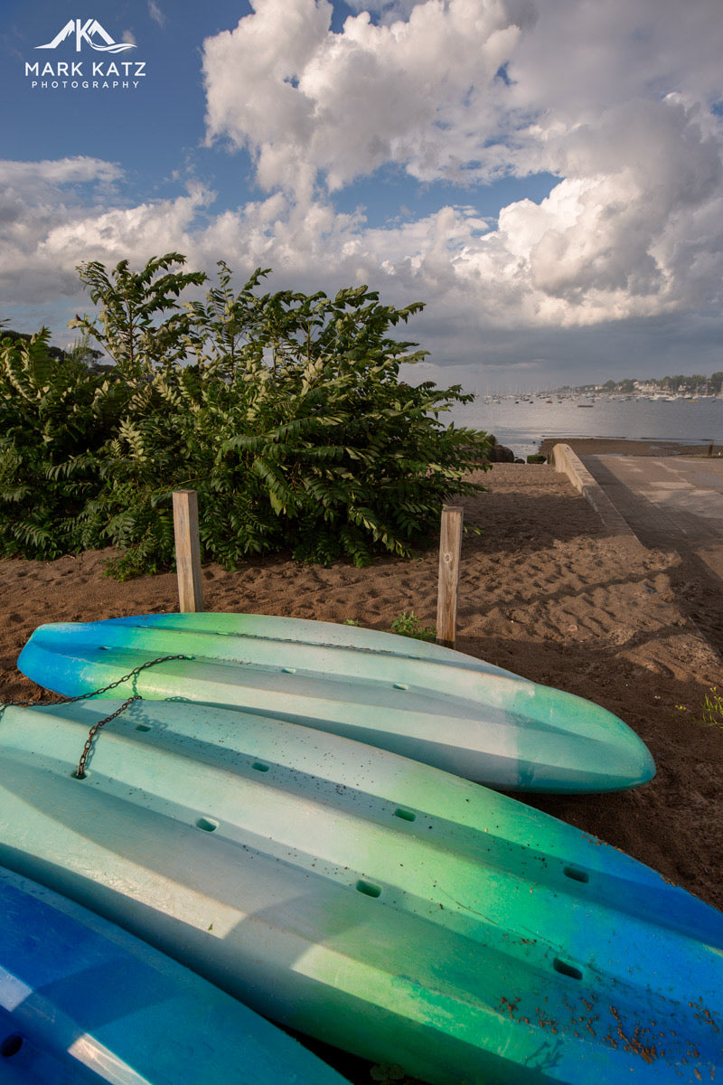 Vibrant kayaks stacked in sunlight, colorful nautical fine art photograph for energetic coastal decor.