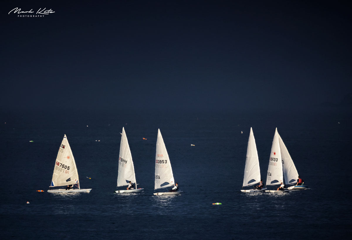 Illuminated sailboats on dark water resembling icebergs, modern maritime fine art photography.
