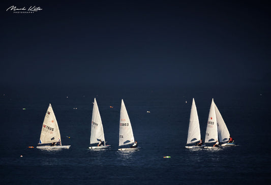 Illuminated sailboats on dark water resembling icebergs, modern maritime fine art photography.