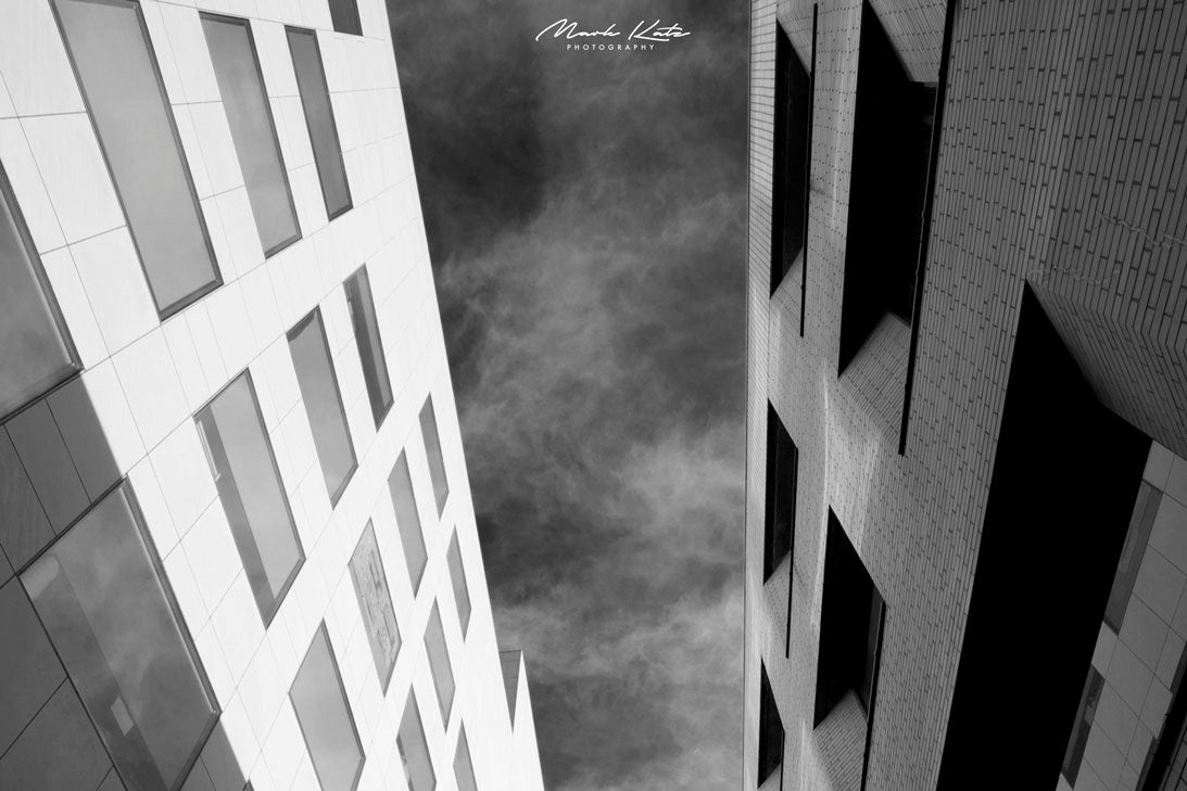 Tall buildings forming geometric sky alley views, urban architectural fine art photography for modern spaces.