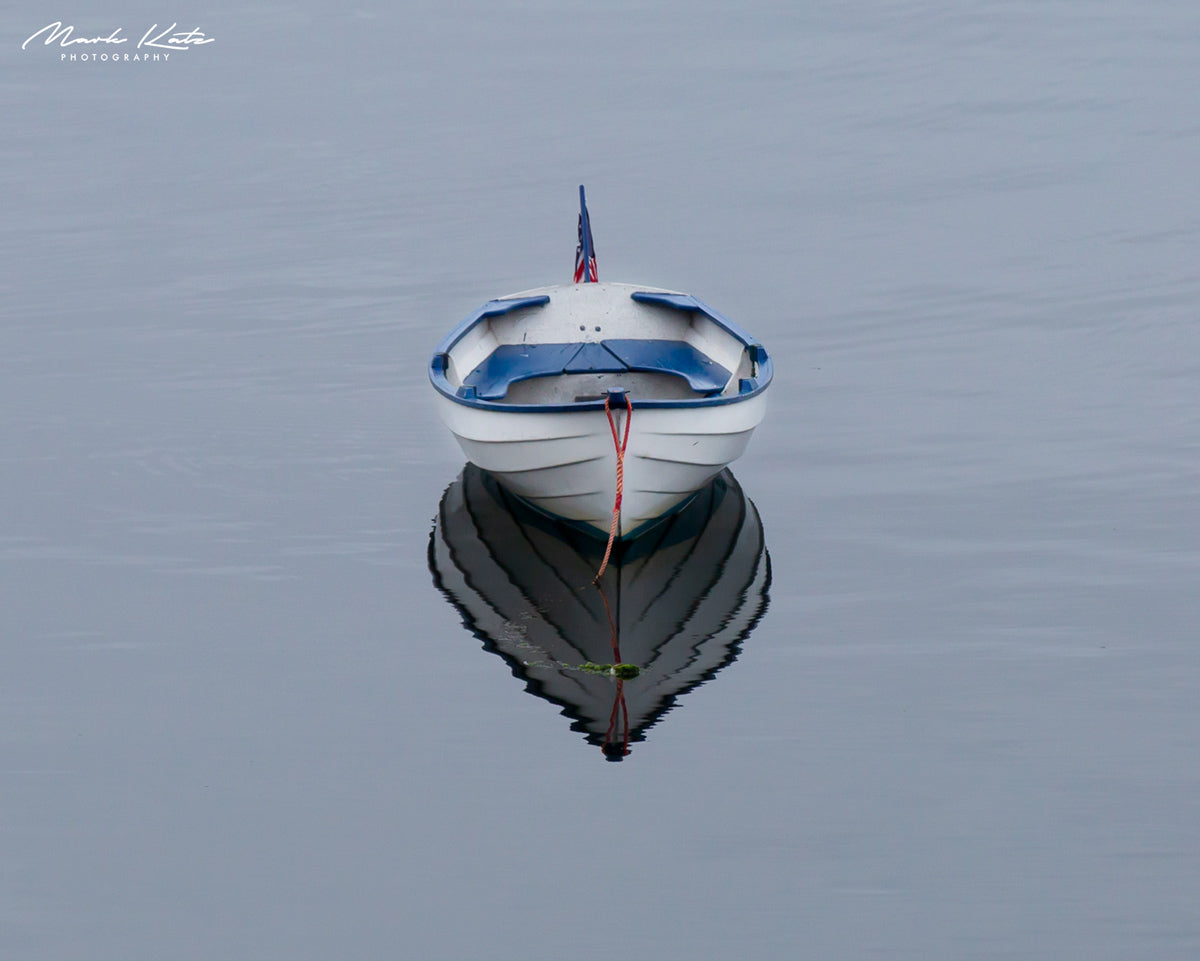 Single sailboat sitting solo and still in calm waters, minimalist nautical fine art photography.