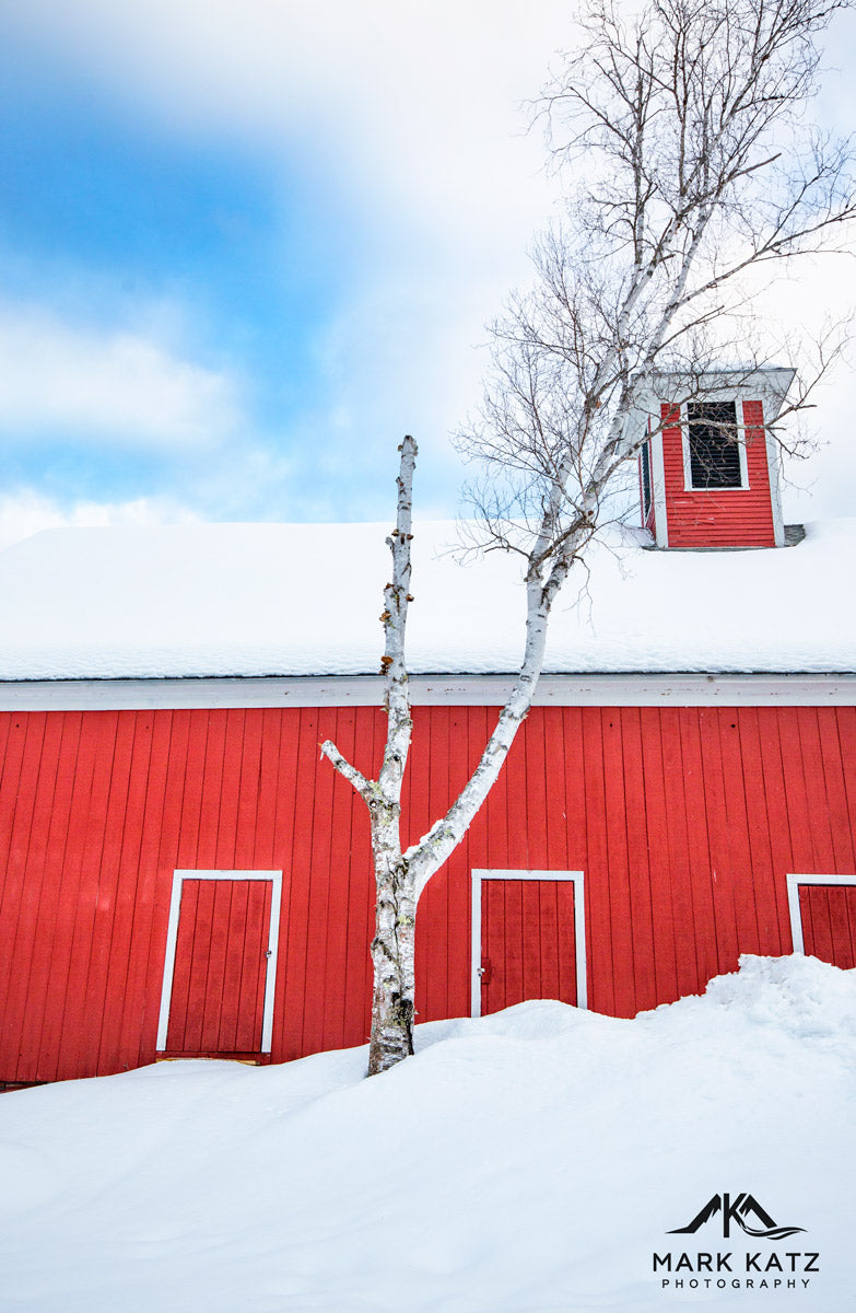 Vibrant red barn under blue sky, classic New England architecture captured in fine art photography.