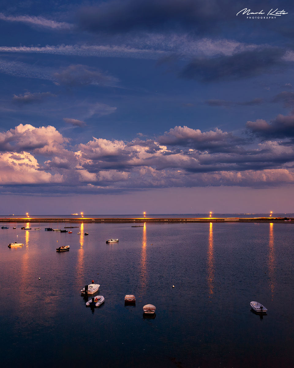Sunset sky casting spotlight glow on clouds over tranquil harbor in dramatic seascape photography.