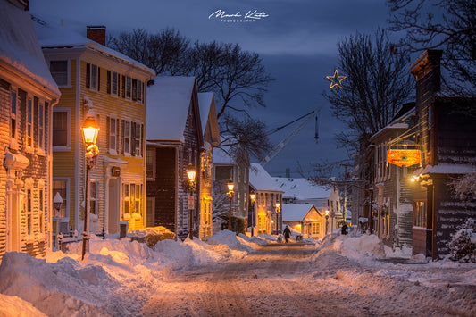 Houses glowing warm while snow piles outside, cozy snowed in fine art photography for winter decor.