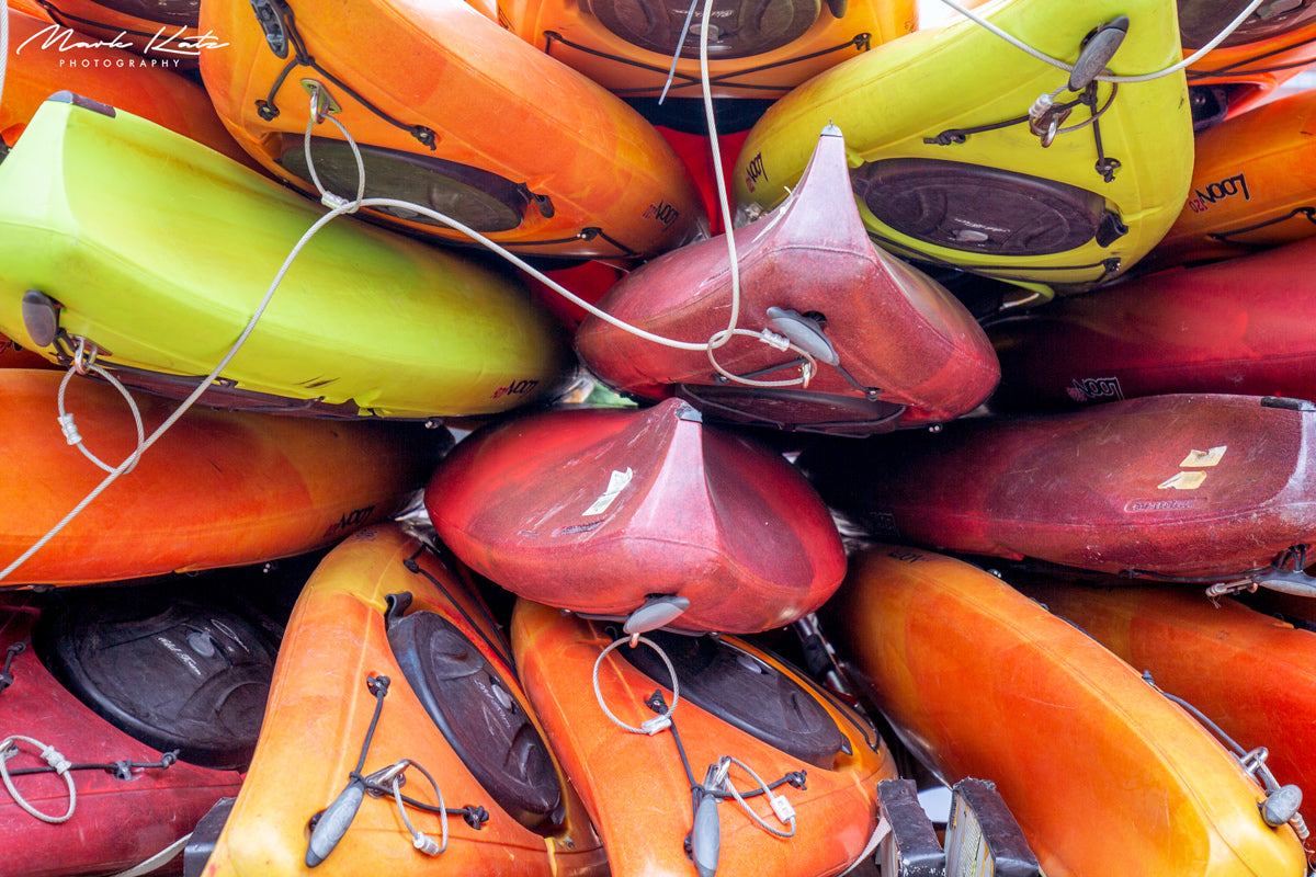 Brightly colored kayaks stacked in lively arrangement, vibrant fine art coastal photography.